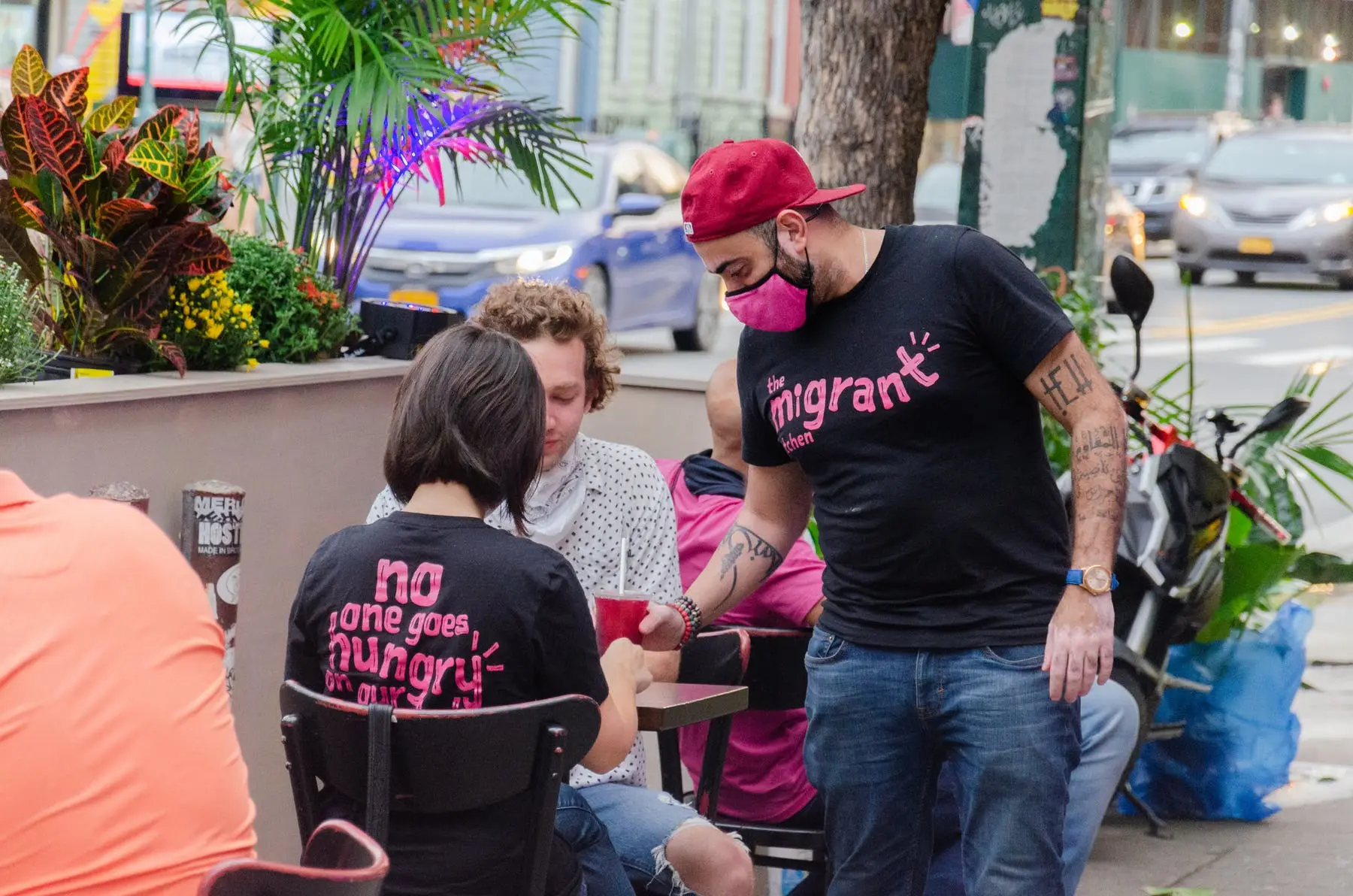 A man and a woman dining at The Migrant Kitchen while an employee serves them food and drinks
