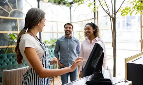 Friendly waitress welcoming a couple to a restaurant and searching for their reservation on the computer