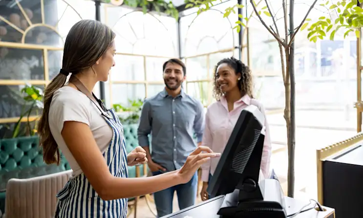 Friendly waitress welcoming a couple to a restaurant and searching for their reservation on the computer