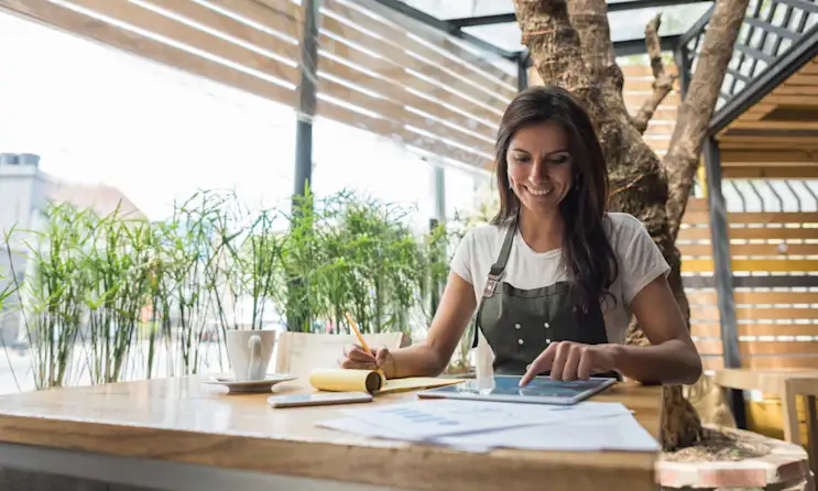 Woman works on her restaurant's finances at a wooden table