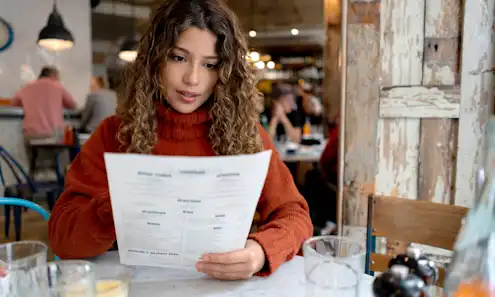 Woman sits at a table in a restaurant and looks over the menu