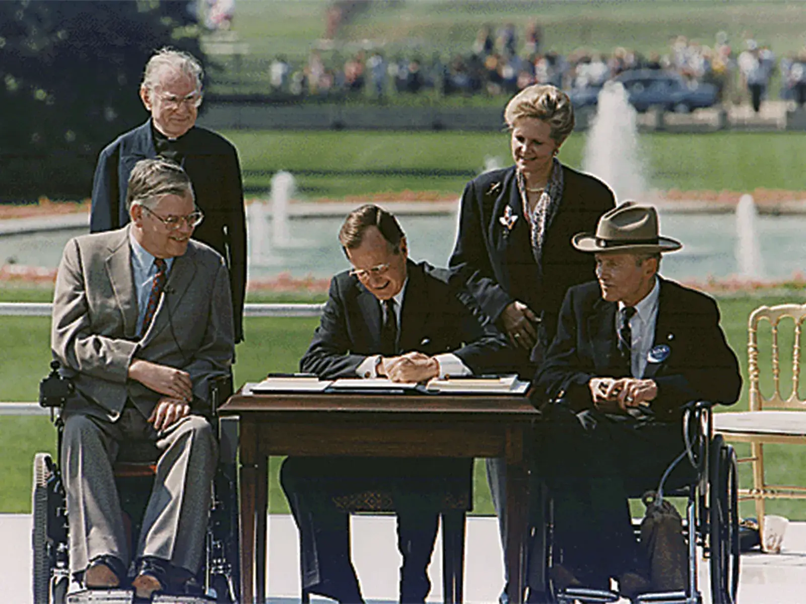 President George H. W. Bush signing the Americans with Disabilities Act in 1990. The president is seated at a table outdoors surrounded by four people, two of whom sit in wheelchairs.